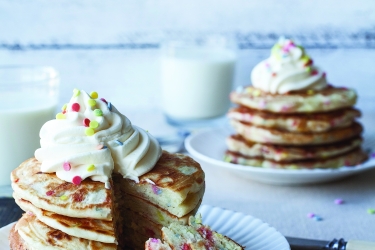 An image of two plates with pancakes covered in whipped cream 