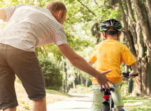man helping child by pushing him on a bike