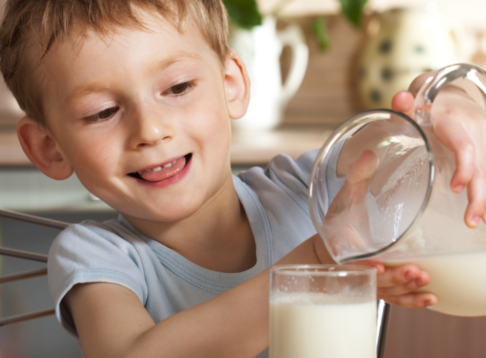 child pouring milk from jar into glass